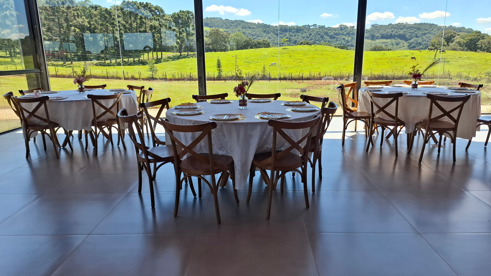 Salão com mesas redondas e vista para o campo