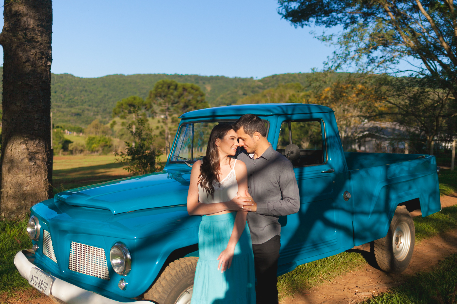 Casal em ensaio ao lado de pickup clássica azul com paisagem de montanhas